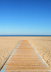 Fototapeta na wymiar Wooden pathway leading to the beach and sea. Summer scene with clear blue sky