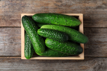 Crate full of fresh ripe cucumbers on wooden background, top view