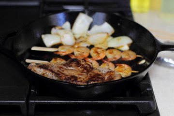 Surf and turf with NY strip and shrimp kabobs with grilled onions, in a cast iron skillet.