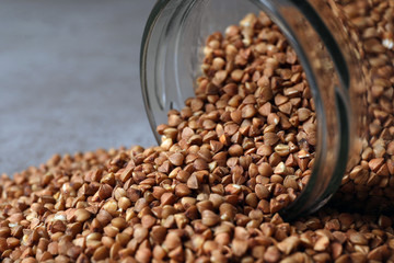 Overturned glass jar with uncooked buckwheat on table, closeup