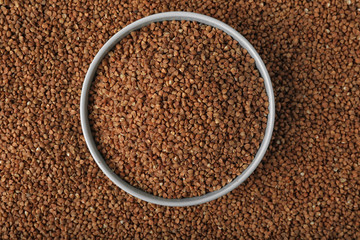 Uncooked buckwheat in bowl on grains, top view
