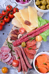Smoked sausages assortment, cheese, nuts, cherry tomatoes, pickled vegetables and olives on the white wooden table. Varied appetizers. Top view