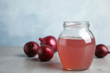 Glass jar of onion syrup and fresh vegetable on table. Space for text