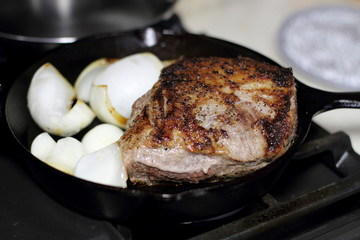 Sirloin steak frying in a cast iron pan with onions on the stove top.