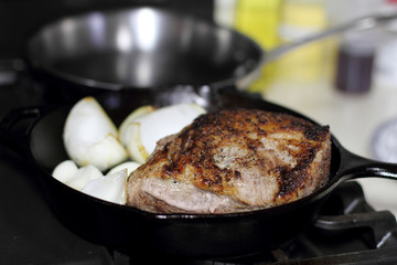 Sirloin steak frying in a cast iron pan with onions on the stove top.