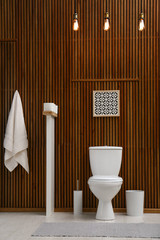 Fototapeta na wymiar White toilet bowl near wooden wall in modern bathroom interior