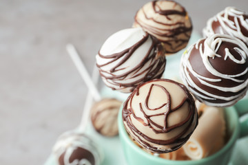 Yummy cake pops coated with chocolate in cup on table, closeup. Space for text