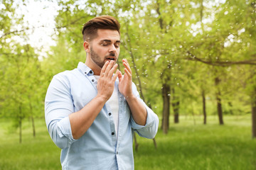 Young man suffering from seasonal allergy outdoors, space for text