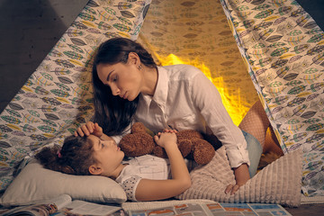 Mother and her daughter are in a teepee tent with some pillows. Happy family.
