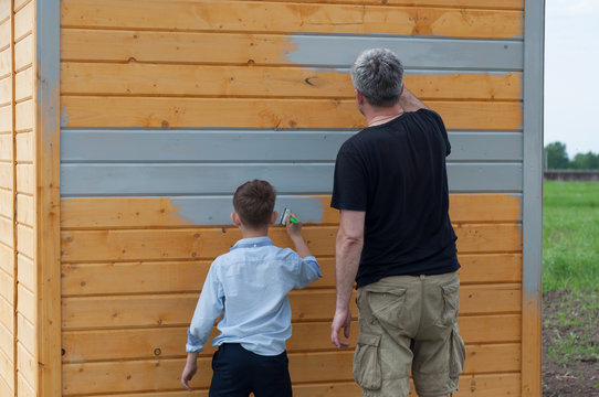 father and son paint a wooden shed with gray paint on the plot