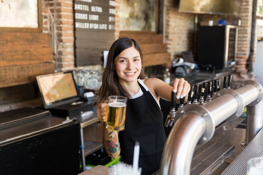 Beautiful female bartender serving a glass of beer