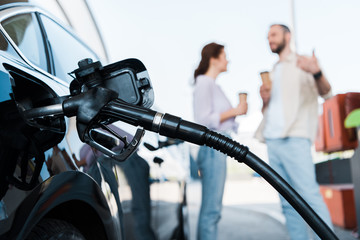 selective focus of black automobile refueling with benzine near man and woman on gas station