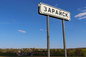 Old road sign with destination city name on blue sky background, Zaraysk, Moscow region, Russia.  The inscription on the plate is translated as "Zaraysk". 