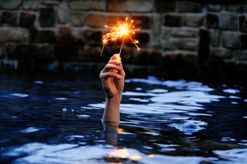4th of July holiday concept with hand holding sparkler fireworks from water at dusk. - Powered by Adobe