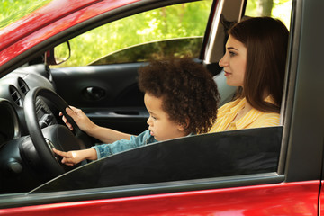 Mother with cute little daughter driving car together. Child in danger