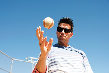 Baseball player in casual attire playing with ball on sunny day outside.