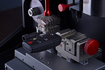 Close view of key copying machine with key. Duplicate machine make new key. Locksmith theme. Blank keys for cutting. Black modern car door opener.