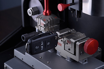 Close view of key copying machine with key. Duplicate machine make new key. Locksmith theme. Blank keys for cutting. Black modern car door opener.