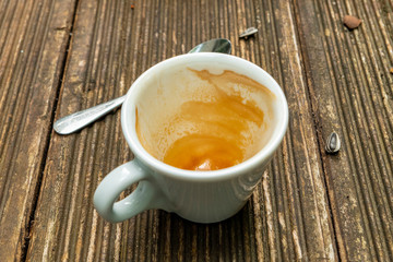 dirty empty espresso cup on a wooden table with coffee crema and spoon