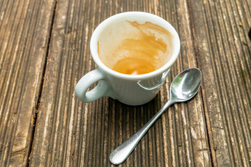 dirty empty espresso cup on a wooden table with coffee crema and spoon