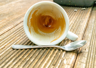 tilted dirty empty espresso cup on a wooden table with coffee crema and spoon