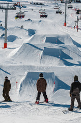 Snowboarders waiting for their turn in front of the kickers in the snowpark