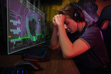 Professional young caucasian gamer playing online on his PC. He upset because of losing the game
