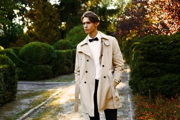 handsome young man in trendy coat and bow tie posing outdoors