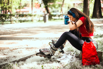 Female takes a break, she drinking water, while listening music on headphones