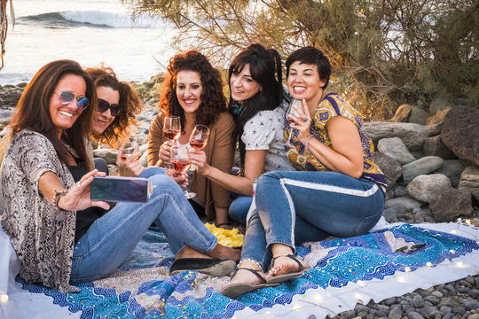 Happy group of people young adult caucasian women having fun outdoor at the beach taking selfie picture and celebrating together with red wine - ladies together laughing a lot