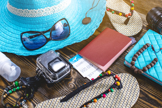 Travel holiday supplies: hat, sunglasses, flip flops, camera passport and airline tickets on old wooden background.