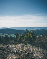 View from the top of a mountain into the valley with clouds in the blue sky and beautiful green trees and lots of rocks