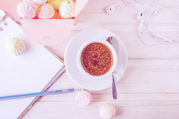 Morning coffee with a notebook and a pencil, with a box filled with small meringues, headphones on a wooden light background.Top view.