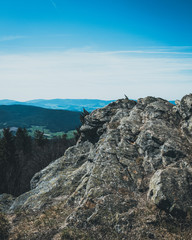 View from the top of a mountain into the valley with clouds in the blue sky and beautiful green trees and lots of rocks