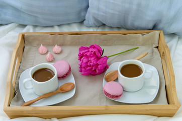 Breakfast in bed for two. Wooden tray with coffee, macaroons and Bizet. Decoration pink peony....