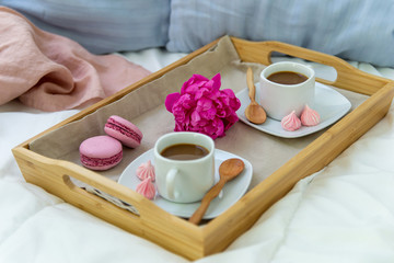 Breakfast in bed for two. Wooden tray with coffee, macaroons and Bizet. Decoration pink peony....
