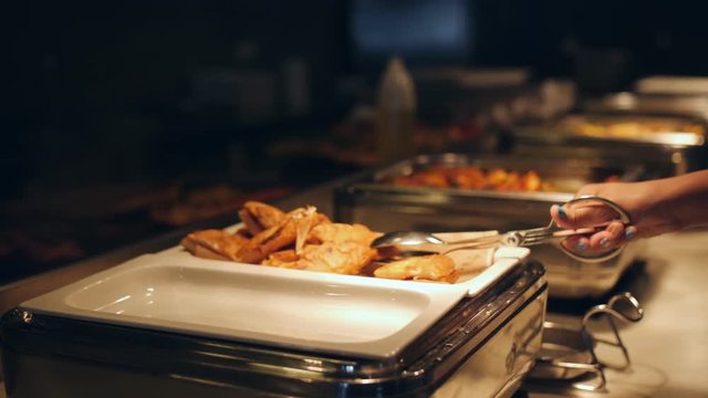 Human hands putting on plate food from buffet table in hotel restaurant close up.