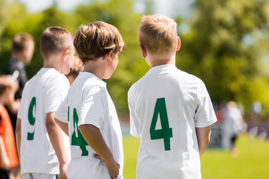 Children Sports Team Members. Junior Soccer Players on Substitution Bench. Kids in White Jersey Shirts with Green Numbers on its Back