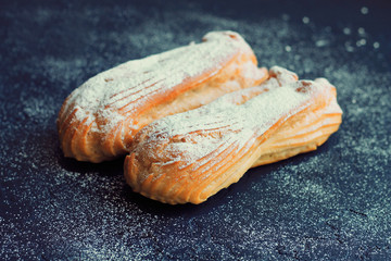 Two eclairs with powder sugar on a dark background.