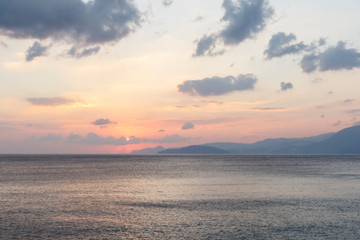 Obraz premium beautiful sunrise over the sea, when the sun begins to rise over the horizon, beautifully illuminating the water and clouds, mountains in the background, a good background image