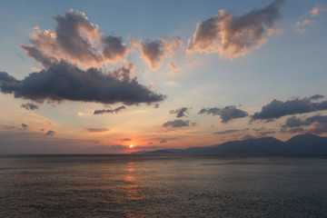 Fototapeta premium beautiful sunrise over the sea, when the sun begins to rise over the horizon, beautifully illuminating the water and clouds, mountains in the background, a good background image