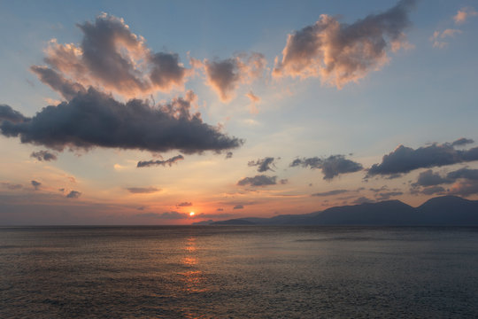 beautiful sunrise over the sea, when the sun begins to rise over the horizon, beautifully illuminating the water and clouds, mountains in the background, a good background image