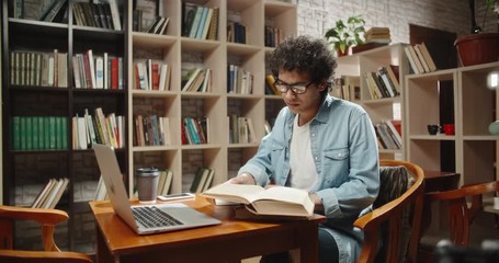 Asian student doing research in library using laptop in books, making a project and preparing for exam. Nerdy guy studying his lessons - education, self-study concept 4k close up - Powered by Adobe