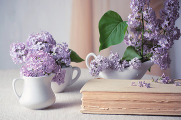 Room interior with lilac flowers in vase and fairytale book on table and curtain hanging on wall