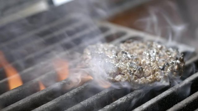 tasty delicious burger patty flipped on hot seared grill pan overhead. A cook is preparing a burger cutlet. Grills meat on the grill. Juicy meat is cooked. Family summer vacation