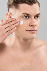 naked young man applying face cream isolated on grey