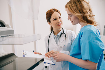 smiling radiologist holding clipboard while standing near patient reading diagnosis on clipboard