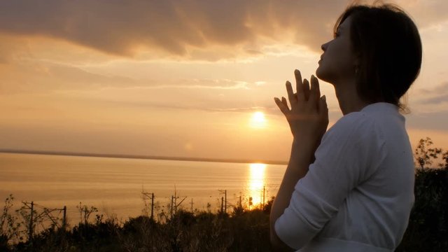 silhouette of young woman figure praying to God at sunset, the girl folded her hands at the chin in the field, concept of religion