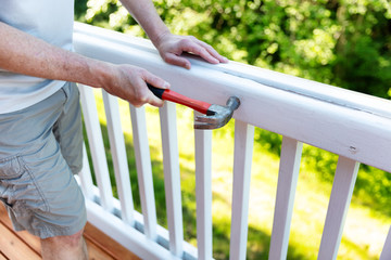 Close up of mature man hammering nail into white railing of outdoor deck