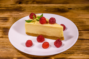 White plate with cheesecake New York, leaf of mint and raspberries on wooden table
